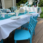 Outdoor setting with blue chairs and white tablecloths on a wooden deck.