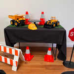 Table with construction-themed toys and safety equipment on a wooden floor.