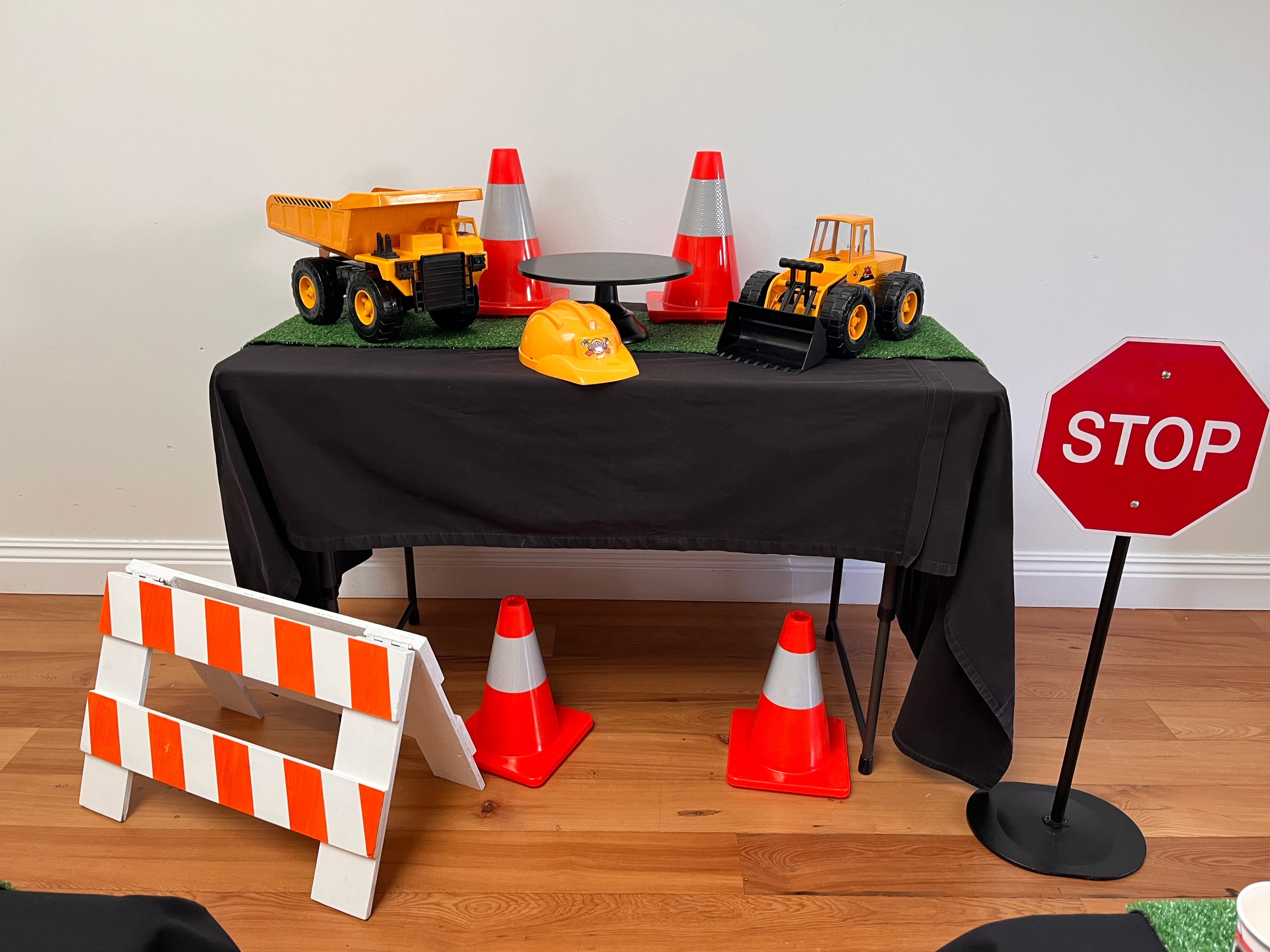 Table with construction-themed toys and safety equipment on a wooden floor.