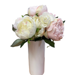 Bouquet of pink and white flowers in a white vase on a wooden surface with a gray background