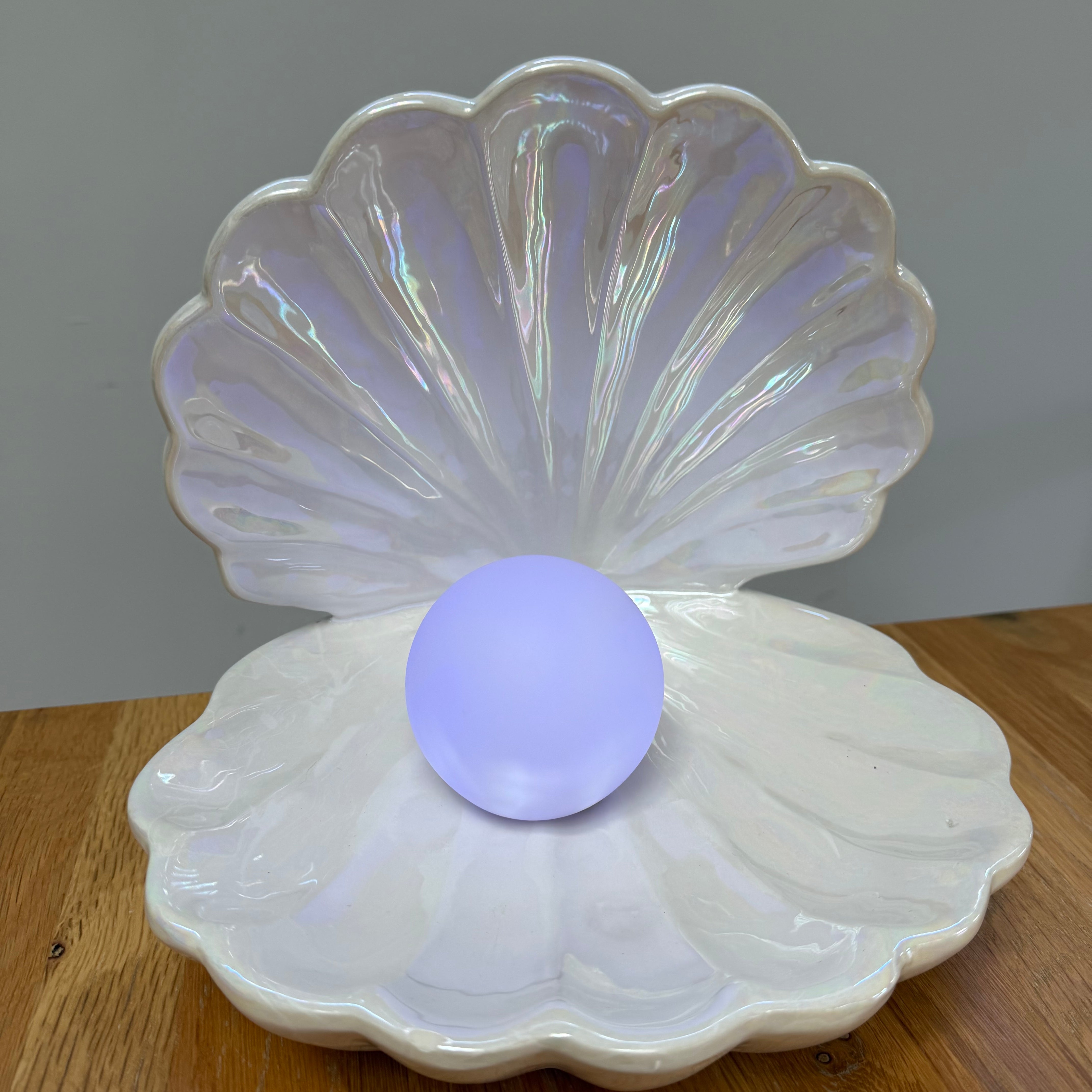 Iridescent shell-shaped container with a purple ball inside on a wooden surface.