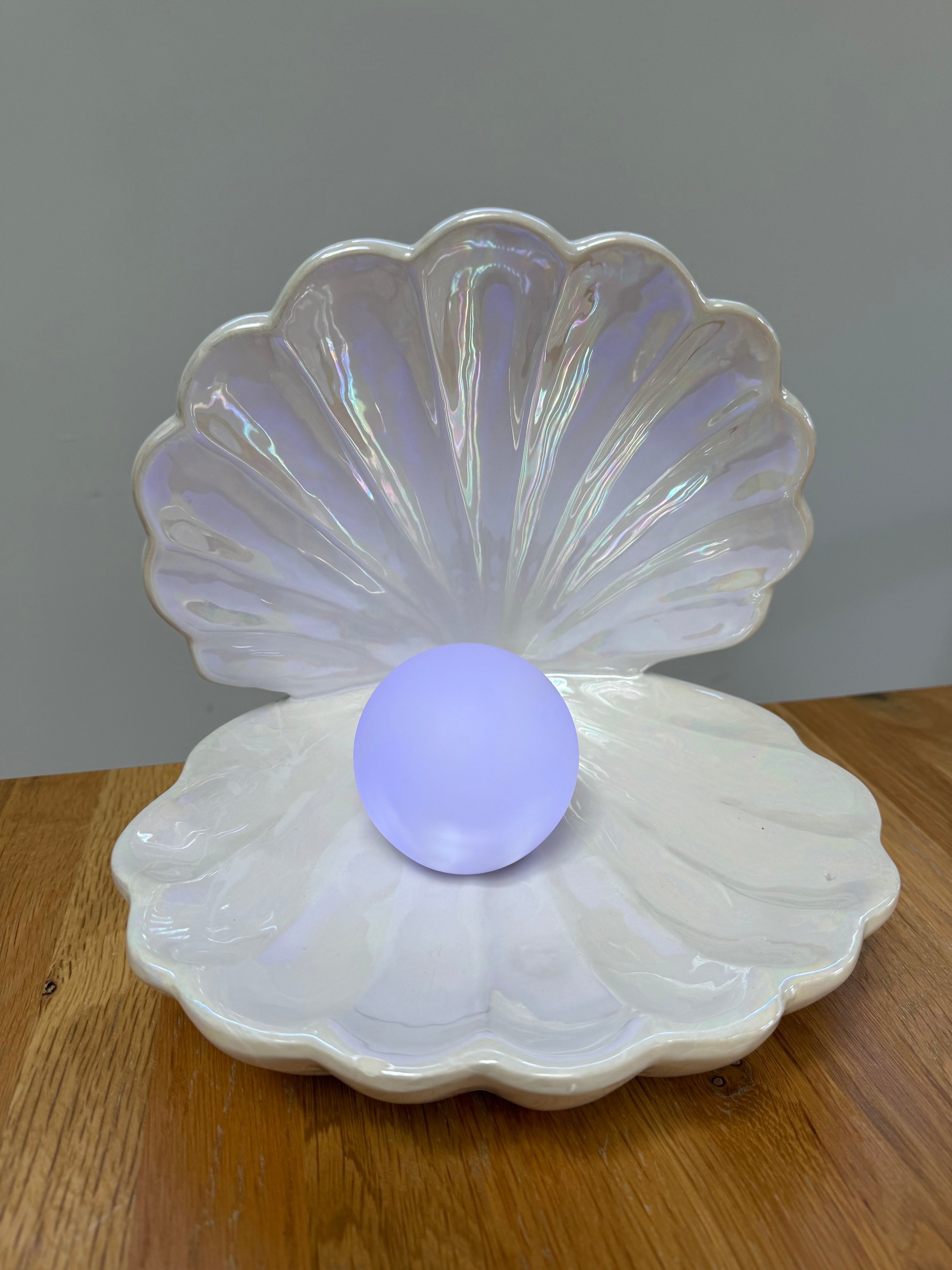 Iridescent shell-shaped container with a purple ball inside on a wooden surface.