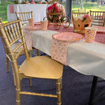 Decorated table with gold chairs and pink tablecloth in an outdoor setting