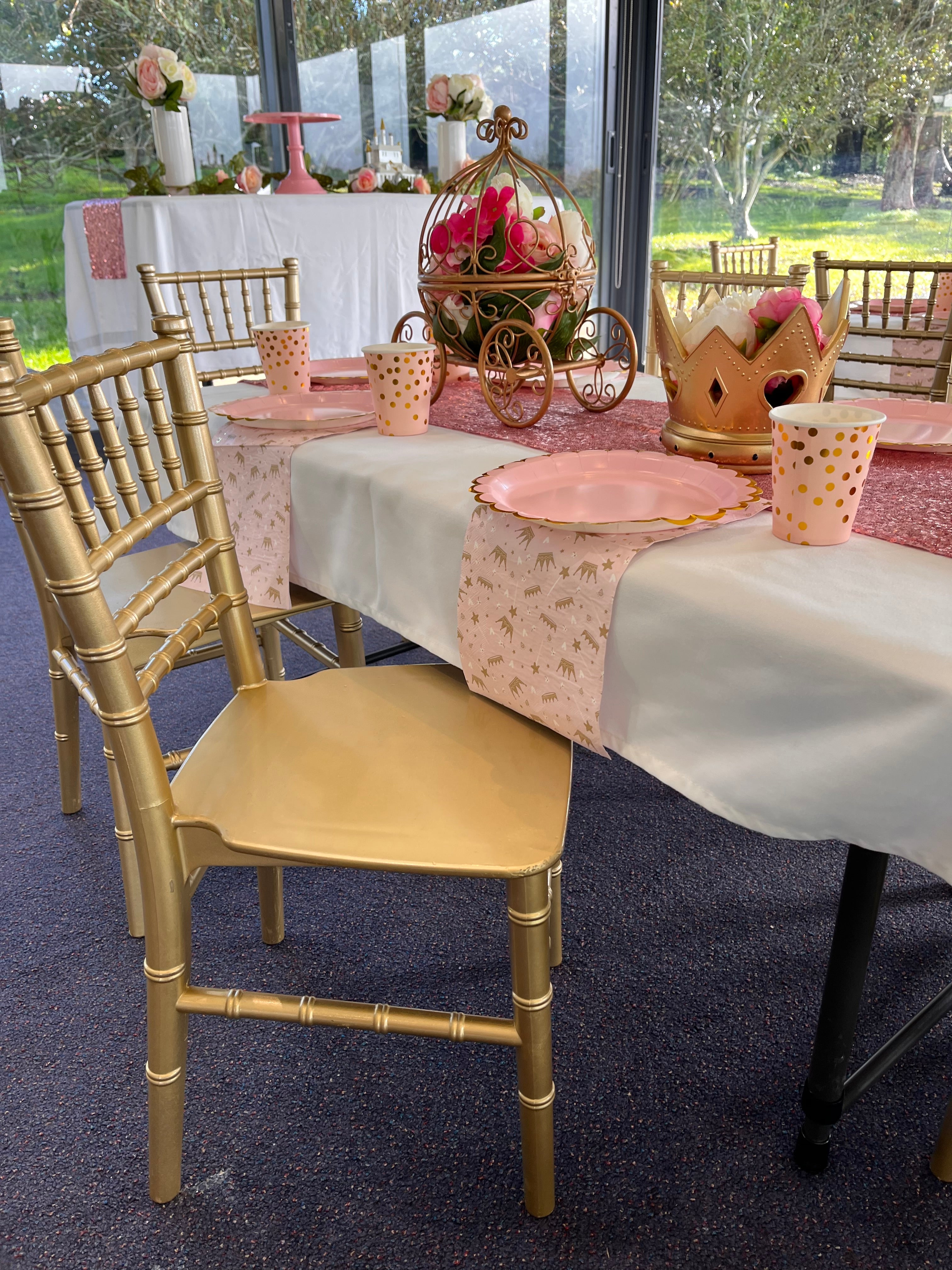 Decorated table with gold chairs and pink tablecloth in an outdoor setting