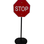 Red stop sign on a black stand against a white wall.