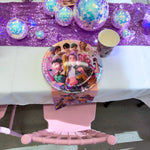 Table setting with decorative plates, balloons, and a purple runner on a white table.