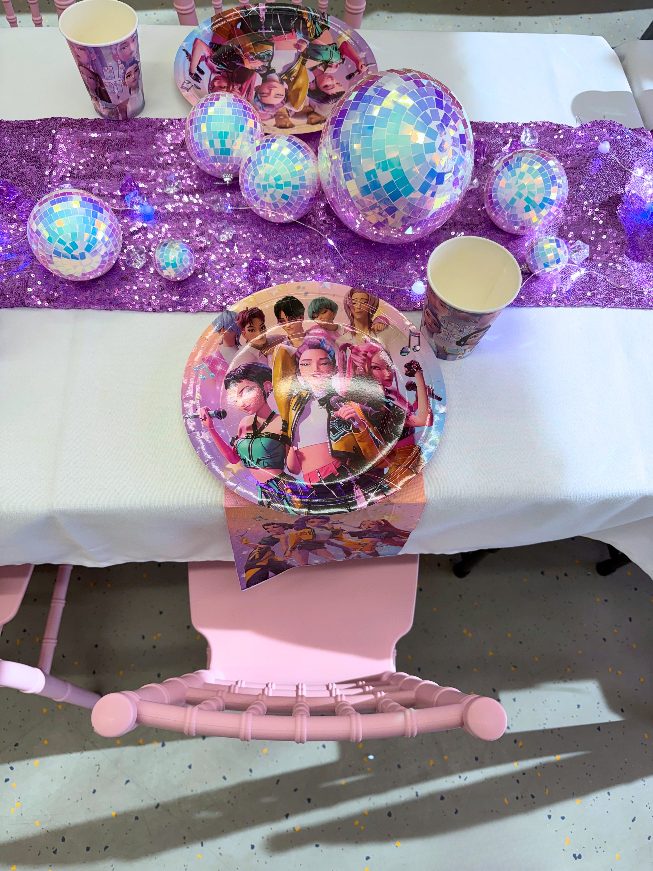 Table setting with decorative plates, balloons, and a purple runner on a white table.