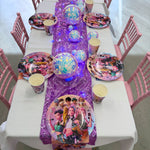 Children's birthday party table setup with colorful plates, cups, and a purple glittery runner.