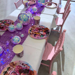 Children's birthday party table setup with pink chairs, colorful plates, and a purple tablecloth.