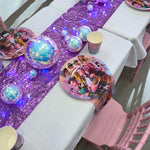 Children's party table setup with purple glitter tablecloth, disco balls, and themed plates.